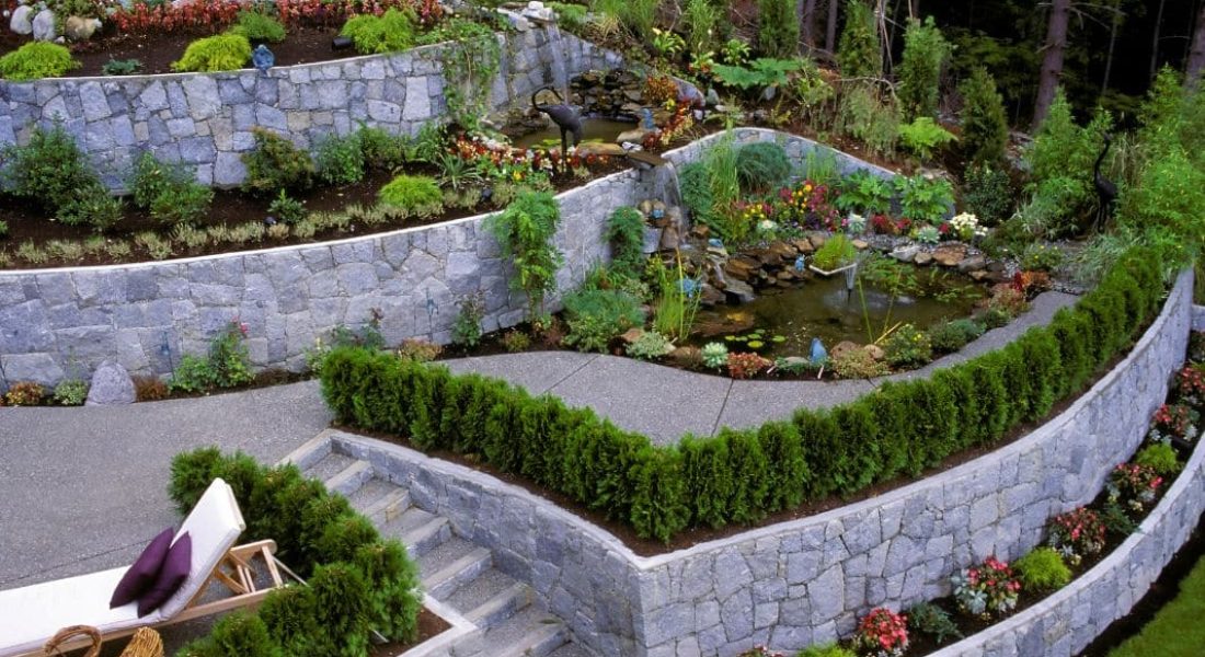 Elevated garden beds with stone retaining walls and a central pond.